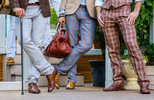 Stylish men in trendy British tweed suits with a walking stick and leather valise stand on the terrace in summer