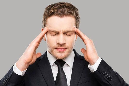 groom stressed having made a mistake touching head with fingers and keeping eyes closed while standing against grey background